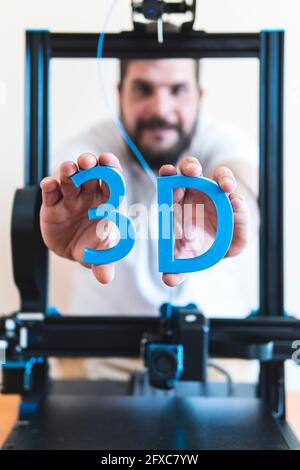 Male technician holding 3D printed text through machinery Stock Photo