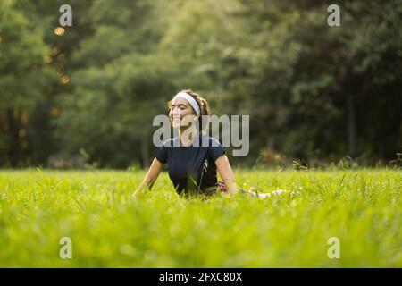 Smiling woman practicing yoga on grass in public park Stock Photo