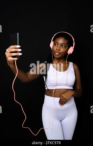 Young woman with headphones taking selfie against black background Stock Photo