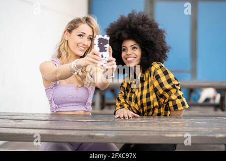 Female friends taking selfie through smart phone at table Stock Photo