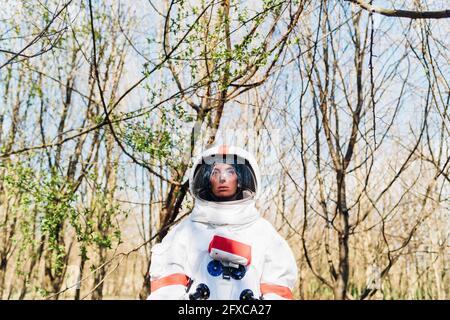 Female astronaut wearing space suit and helmet standing in forest Stock Photo