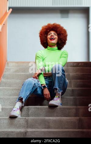 Happy woman laughing while sitting on staircase Stock Photo