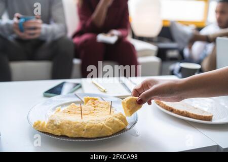 Businesswoman having Spanish omelet at table with colleagues in background Stock Photo