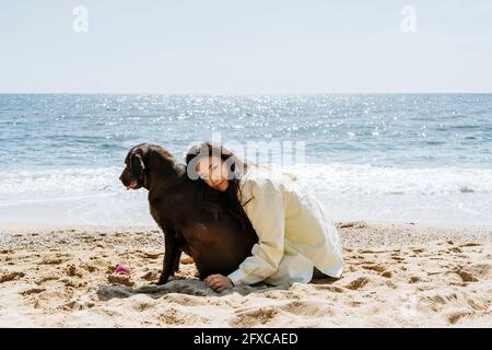 Woman embracing Labrador dog on sand at beach Stock Photo