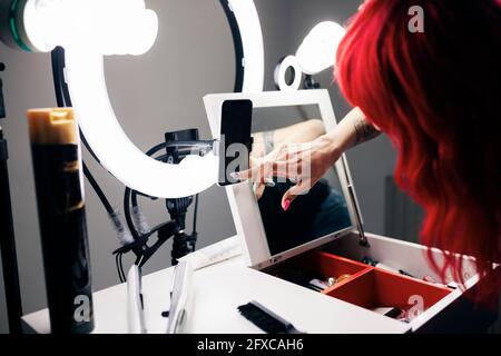 Dyed haired female stylist using smart phone while vlogging at studio Stock Photo