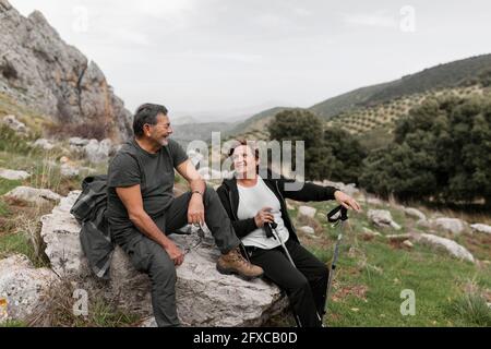 Senior couple hiking in the mountains smiling while sitting on rock Stock Photo