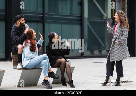 Male and female friends waving hand to each other on footpath Stock Photo