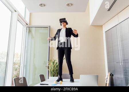 Young businesswoman using virtual reality simulator while standing on desk in office Stock Photo