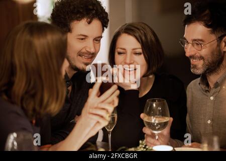 Mature woman showing mobile phone to male and female friends during celebration at home Stock Photo