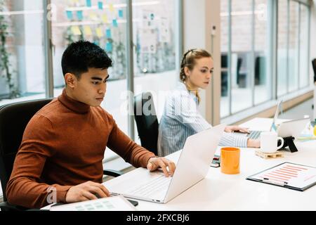 Male entrepreneur working on laptop by colleague at office Stock Photo