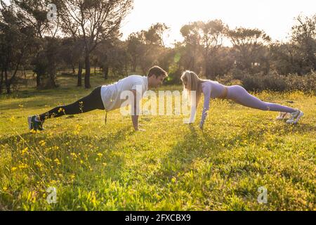 Male and female athlete doing push-ups together on grass area Stock Photo