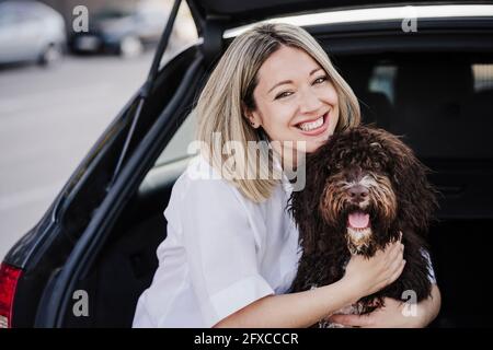 Happy woman embracing Spanish Water Dog in car trunk Stock Photo