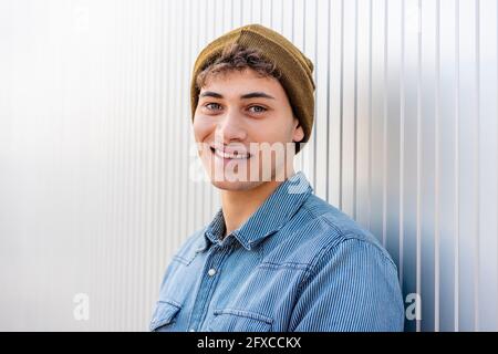 Smiling man wearing knit hat by silver colored wall Stock Photo