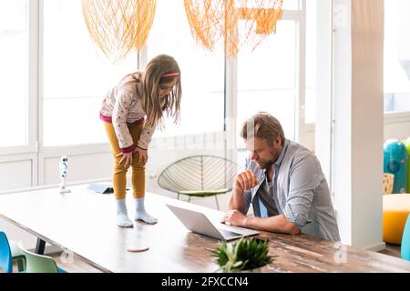 Businessman using laptop by daughter standing on table at home Stock Photo