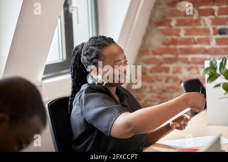 Smiling businesswoman with braided hair looking at document in coworking office Stock Photo