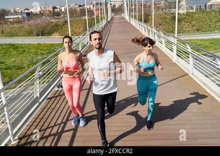 Male and female athletes looking away while running on bridge during sunny day Stock Photo