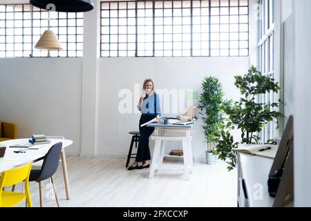 Smiling mid adult businesswoman leaning at desk in office Stock Photo
