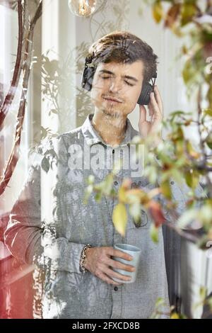 Businessman with eyes closed listening music while having coffee seen through glass Stock Photo