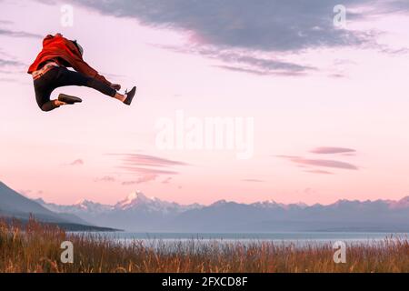 New Zealand, Canterbury, Rear view of young man jumping over Lake Pukaki at sunset Stock Photo