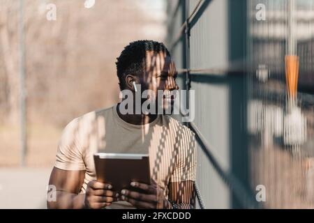 Young man looking away while holding digital tablet during sunny day Stock Photo