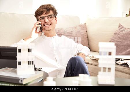 Smiling male architect talking on mobile phone while sitting at sofa Stock Photo