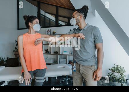 Male physiotherapist and female patient greeting with elbow bump in practice during pandemic Stock Photo