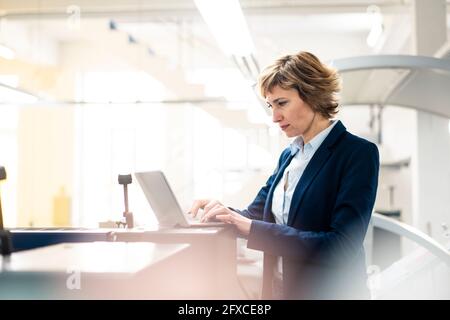 Mature female entrepreneur using laptop while working at industry Stock Photo