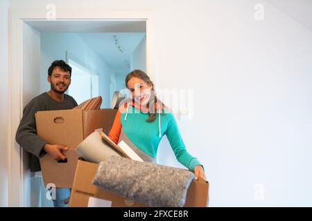 Smiling young couple carrying cardboard boxes while standing at doorway Stock Photo