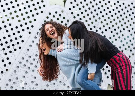 Cheerful female friends playing by wall Stock Photo