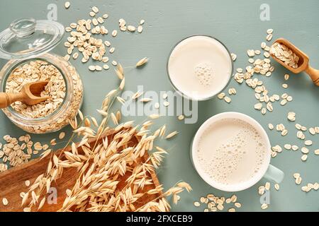 Oat milk in a glass and mug on a blue background. Flakes and ears for oatmeal and granola on a wooden plate. Stock Photo