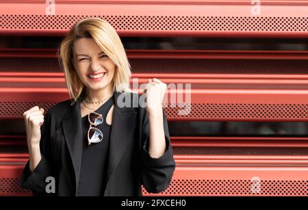 Excited woman clenching fists in front of corrugated wall Stock Photo