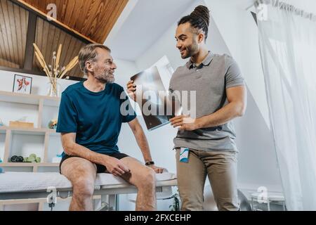 Male physical therapist discussing x-ray image of knee with patient at massage table Stock Photo