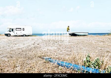 Man on the beach near the boat and white camper parked by the sea. Tourist season on the mediterranean sea. Sicily. Ionian Sea. Stock Photo