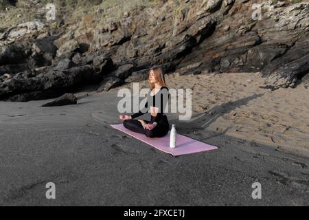 Young woman meditating while sitting on exercise mat at beach Stock Photo