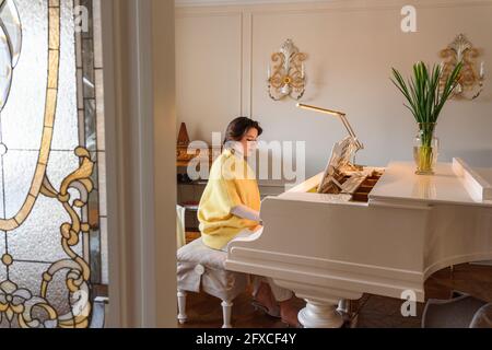 Young woman playing grand piano at home Stock Photo