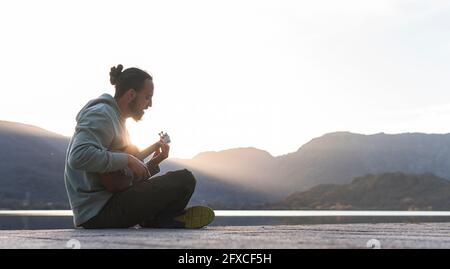 Young man singing while playing ukulele on promenade during sunny day Stock Photo