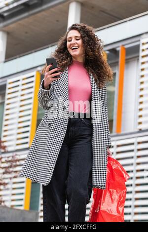 Happy woman walking while using mobile phone Stock Photo