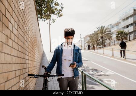 Handsome man using mobile phone while standing with bicycle on footpath Stock Photo