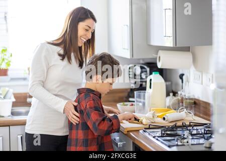 Smiling mother assisting son cutting banana in kitchen at home Stock Photo