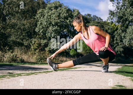 Mid adult woman stretching on footpath in forest during sunny day Stock Photo