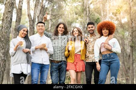 Cheerful male and female friends holding reusable glass in forest Stock Photo