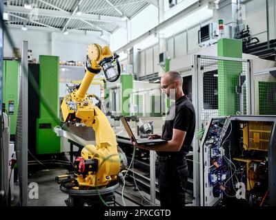 Male engineer using laptop by robotic arm Stock Photo