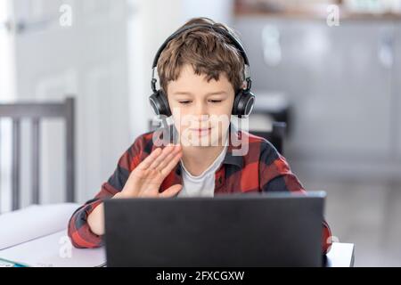 Cute boy waving during video call through laptop at home Stock Photo