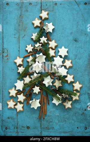 Christmas cinnamon star shaped cookies together with cinnamon and needle branches arranged in Christmas Tree on blue rustic wooden background Stock Photo