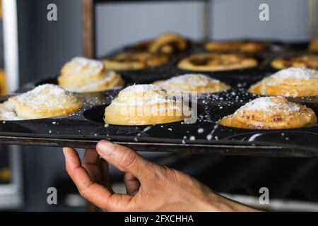 Female baker holding tray of cinnamon buns in kitchen Stock Photo