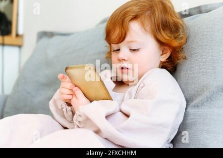 Cute redhead girl using mobile phone on sofa in living room Stock Photo