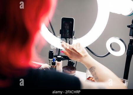 Female vlogger using mobile phone connected at ring light in studio Stock Photo