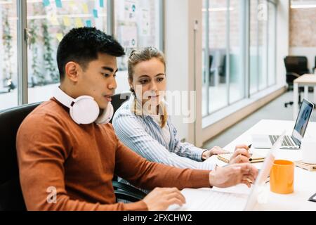 Male and female colleagues discussing over laptop at office Stock Photo