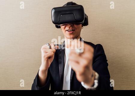 Businesswoman with virtual reality headset gesturing while standing in front of wall Stock Photo
