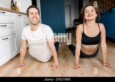 Young happy smiling couple doing yoga exercises on the modern kitchen floor, doing urdhva fly shvanasana exercise, dog face up poses workout wearing Stock Photo